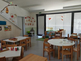 Kindergartengruppenraum mit Spieltischen, verschiedenen Spiel- und Lernmaterialien sowie Kinderarbeiten an den Wänden.